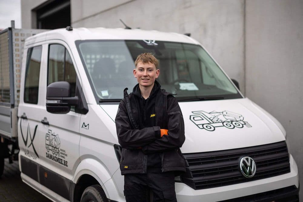 Afbeelding van Willem voor zijn bus, met een glimlach op zijn gezicht.